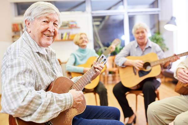 Cheerful senior man playing guitar in a guitar course at the community college